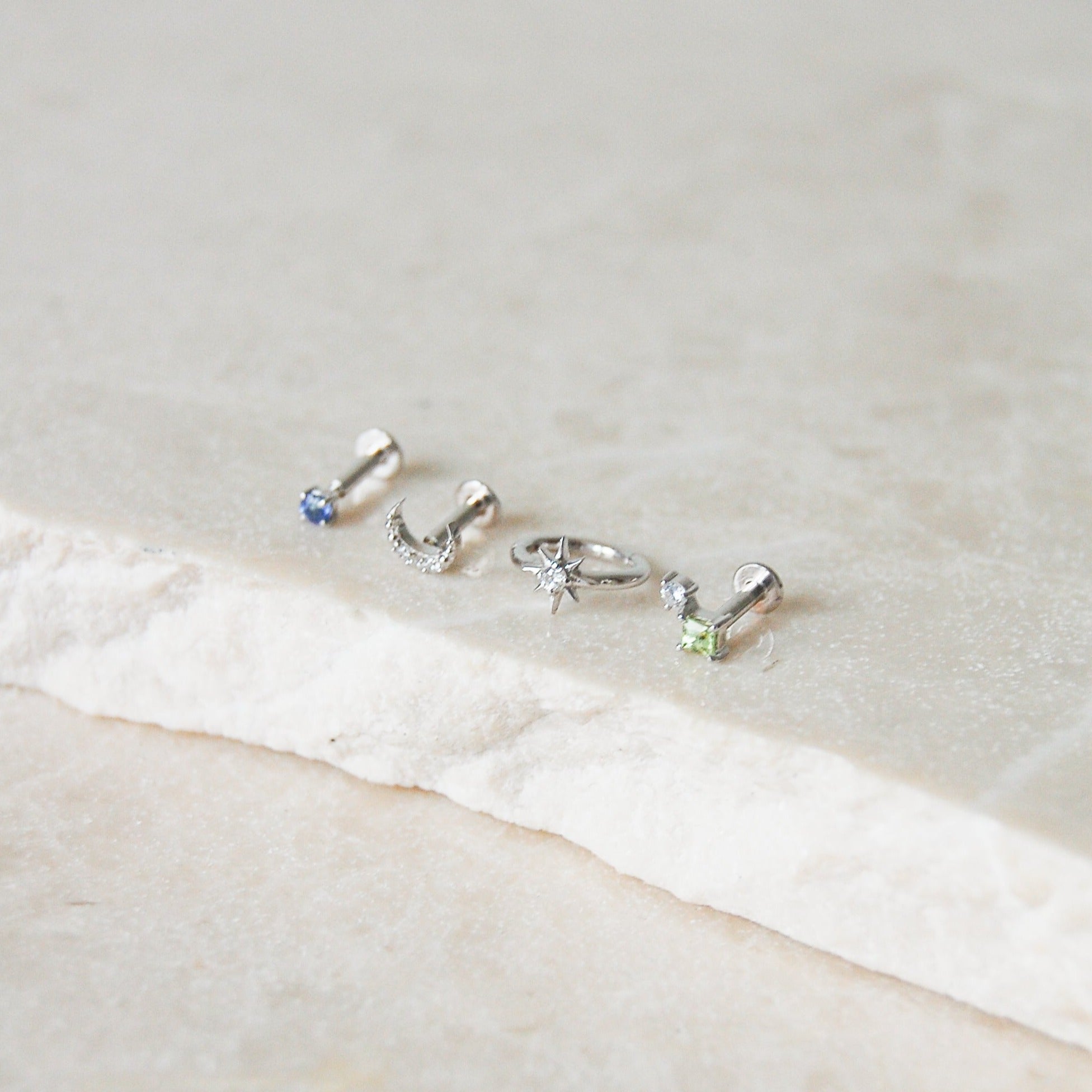 white gold earring display on marble surface including the Diamond North Star Seamless Huggie Hoop Earring White 9k Gold