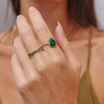 Close-up of a hand wearing a green gemstone ring with a blurred background
