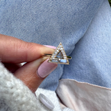 Triangle-shaped ring with gemstones held by a hand against a denim background