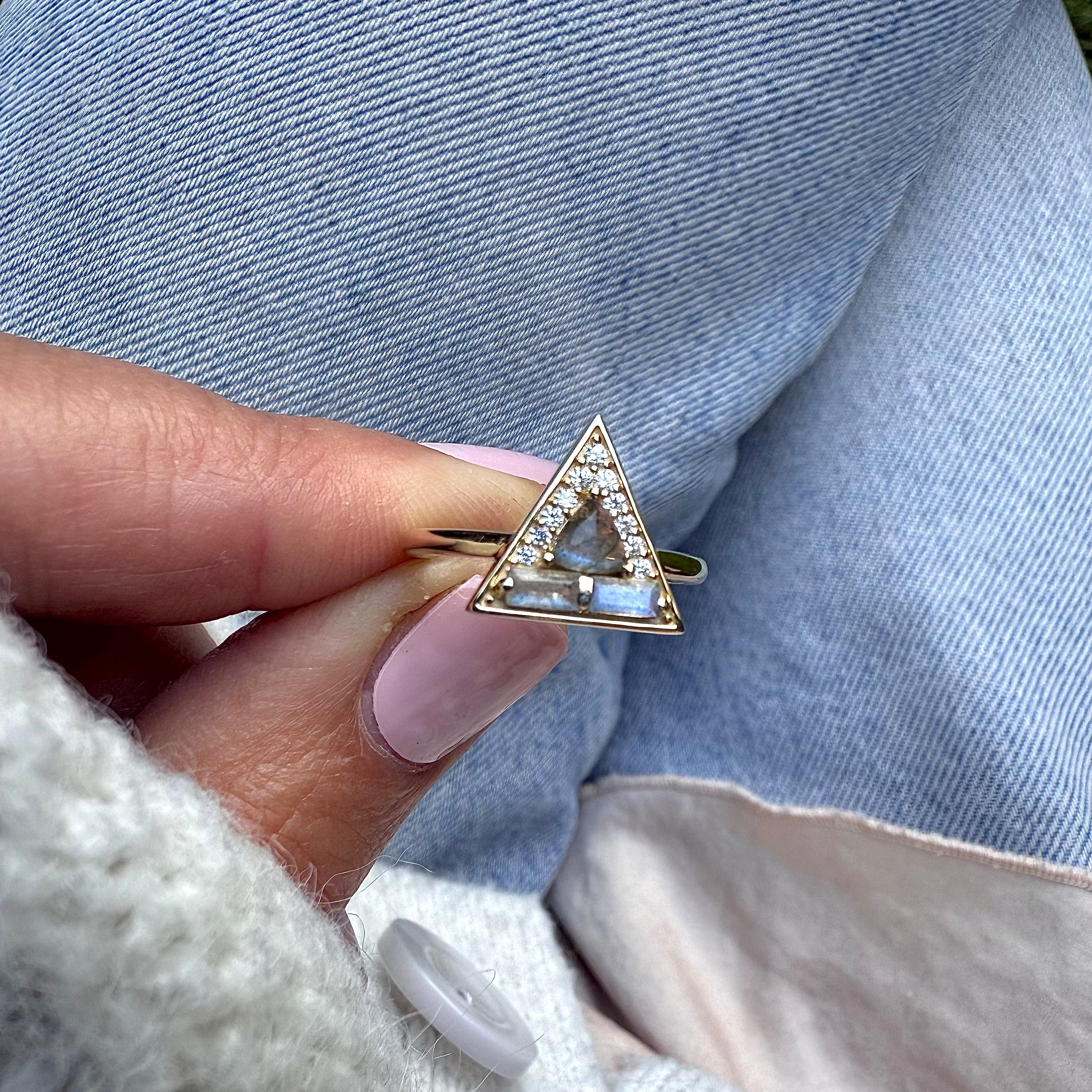 Triangle-shaped ring with gemstones held by a hand against a denim background