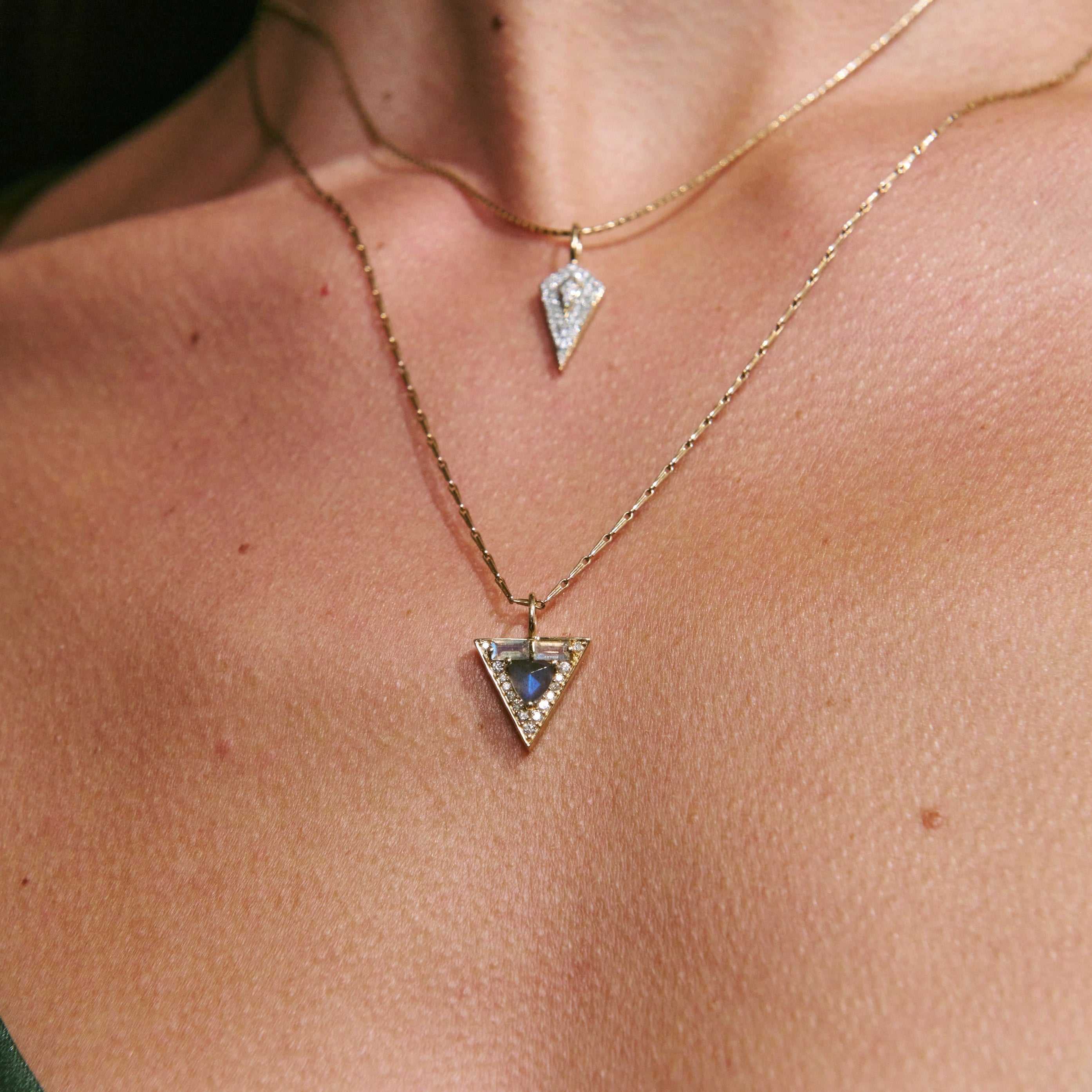 Close-up of a person wearing two gold necklaces with triangular pendants.