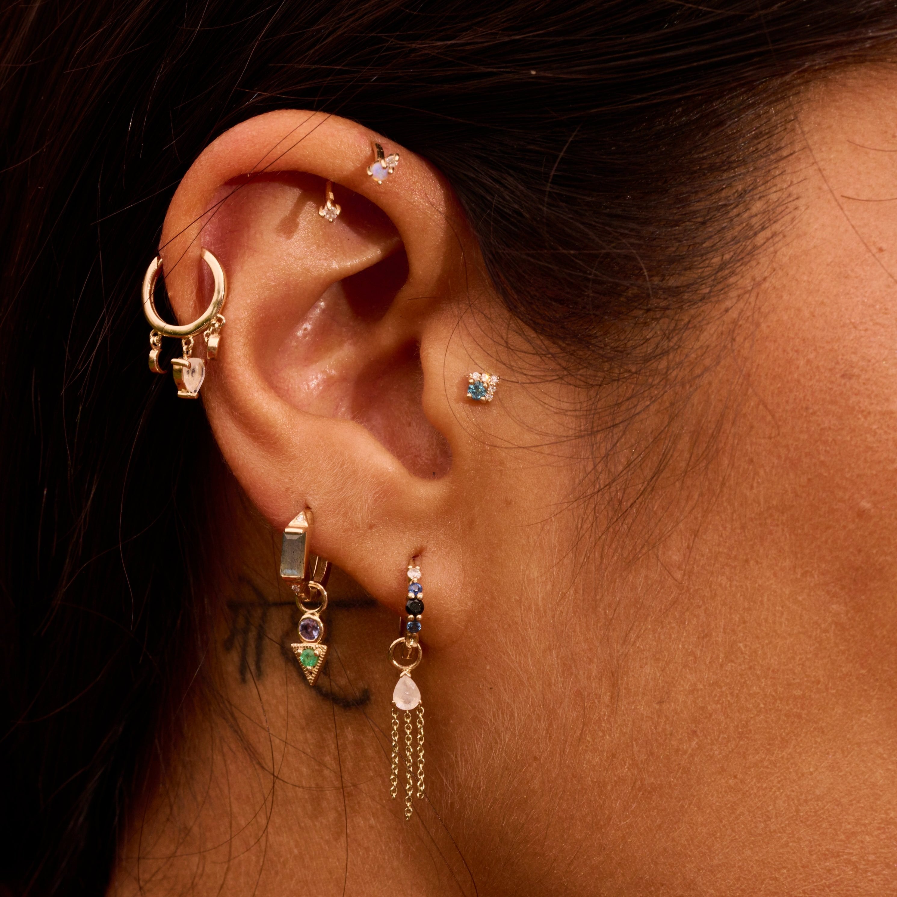 close up of model ear wearing solid gold earrings including the London Blue Topaz & Diamond Arrow Flat Back 9k Gold