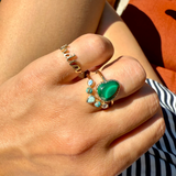 Close-up of a hand wearing two rings with green and blue gemstones.