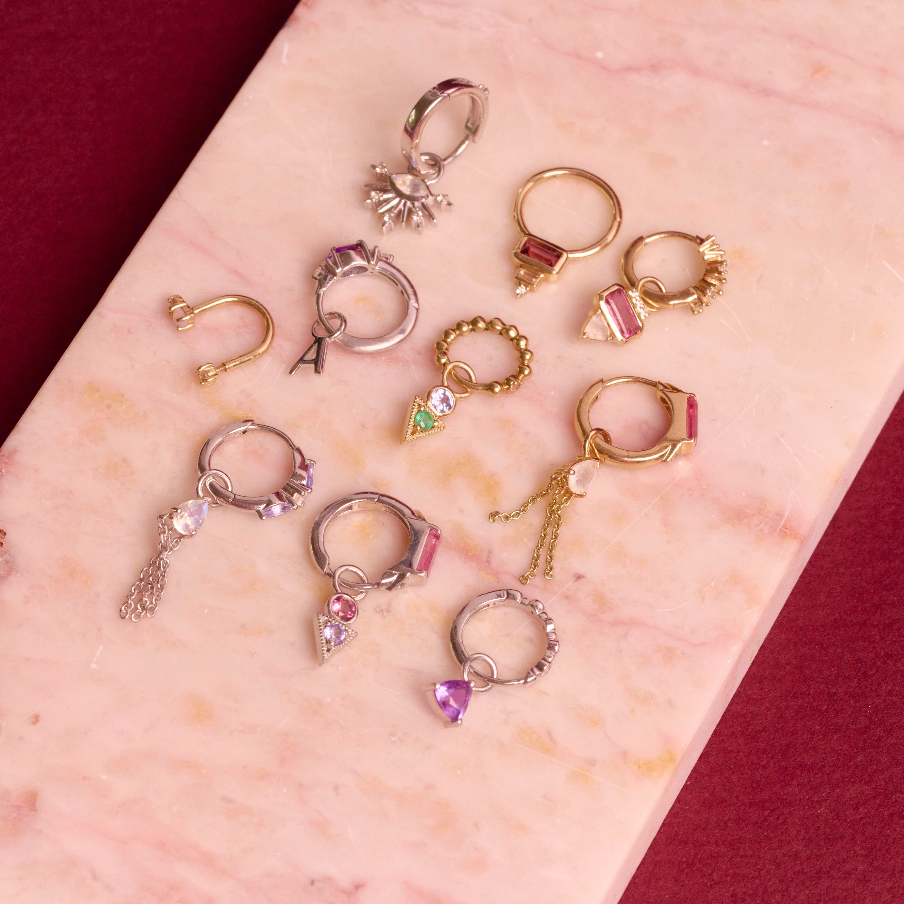 solid metal huggies and earring charms on hard surface including the Pink Tourmaline, Diamond & Moonstone Earring Charm 9k Gold