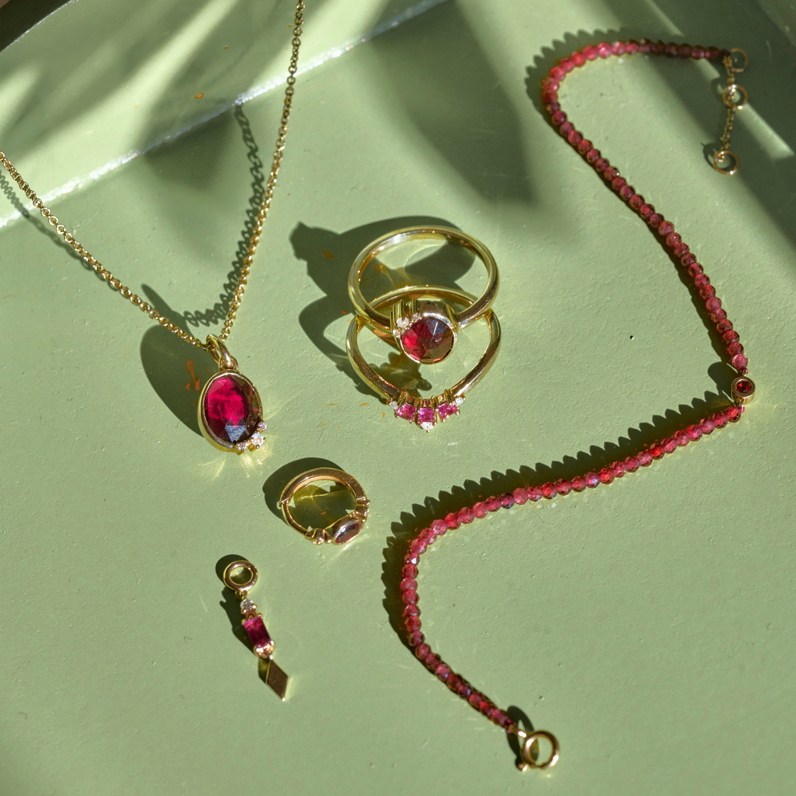 solid gold rhodolite garnet pieces displayed on green tray including the Rhodolite Garnet, Moonstone & White Sapphire Necklace 9k Gold
