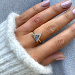 Hand wearing a gold ring with a triangular stone against a denim background