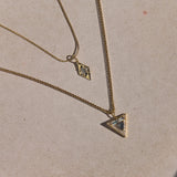 Gold necklace with a triangle pendant on a beige plate