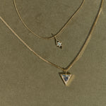 Two gold necklaces with star and triangle pendants on a green background
