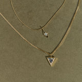 Two gold necklaces with star and triangle pendants on a green background