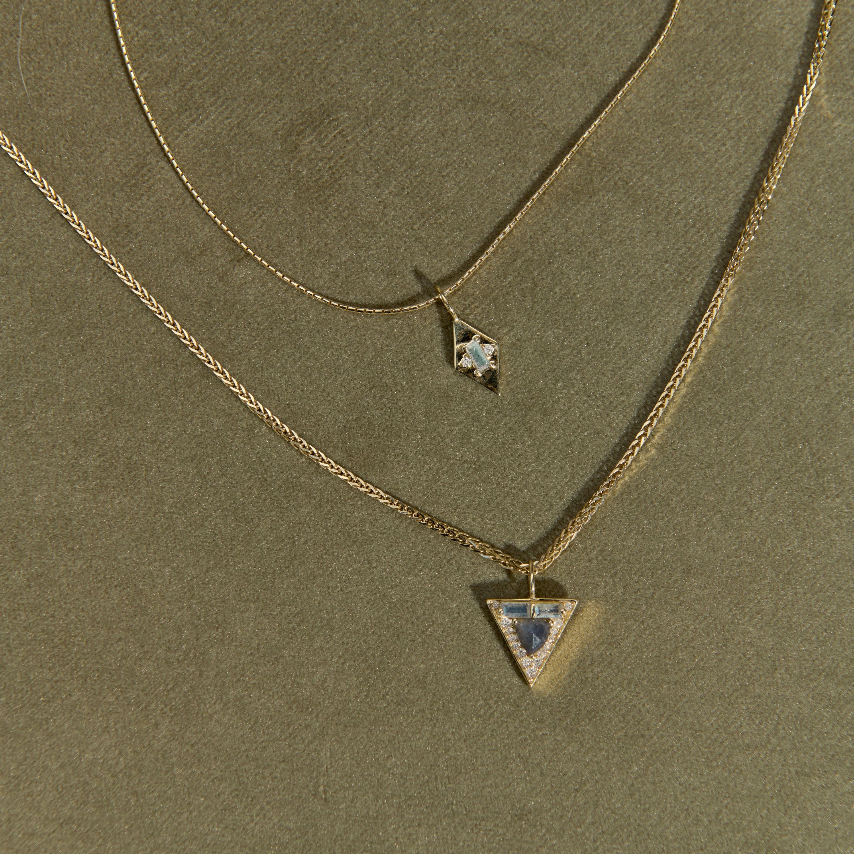 Two gold necklaces with star and triangle pendants on a green background