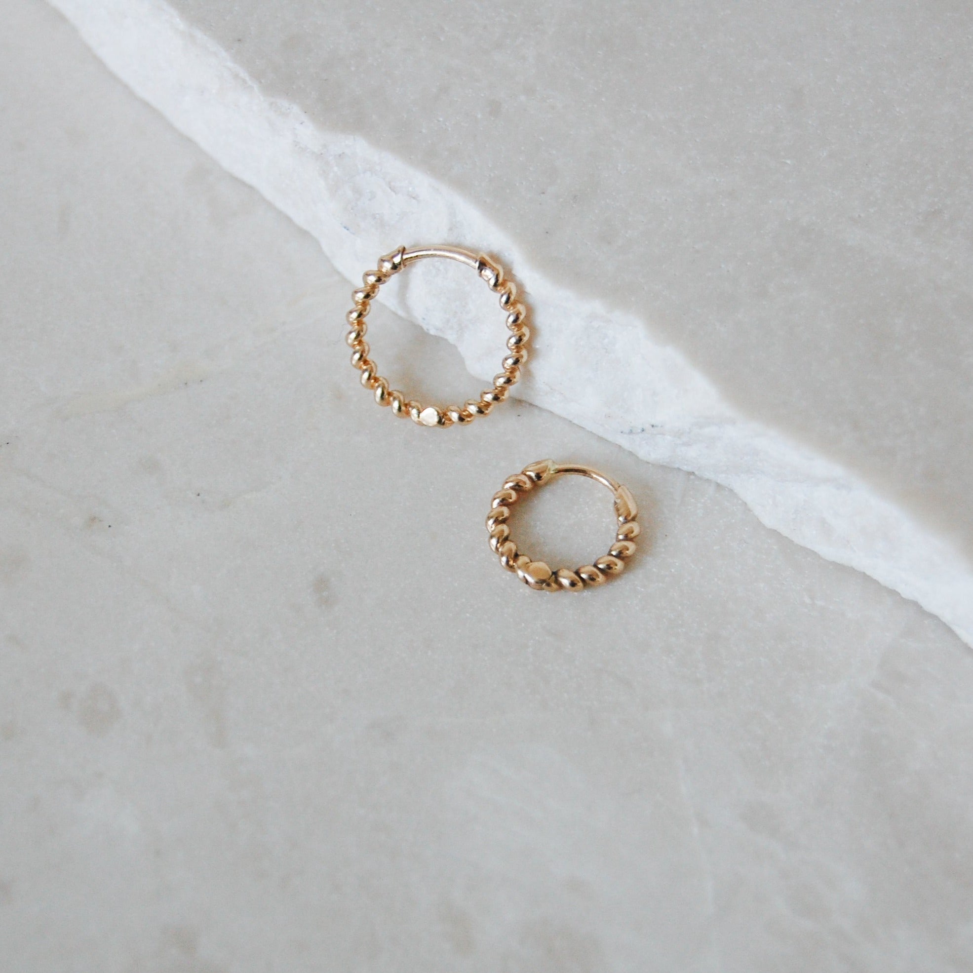 Medium and huggie Twisted Huggie Hoop Earring 9k Gold on marble surface