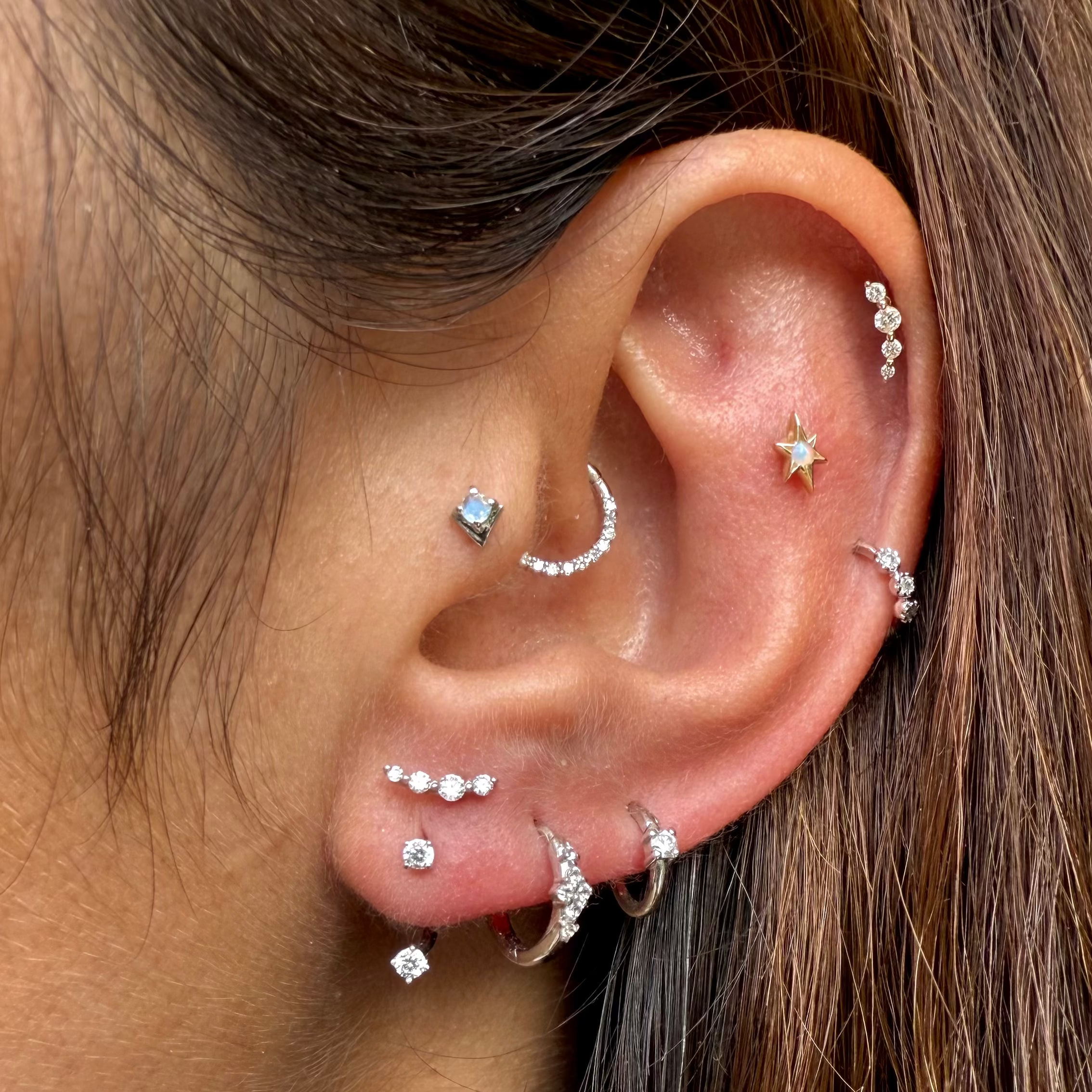 Close-up of an ear with multiple earrings on a person with brown hair.