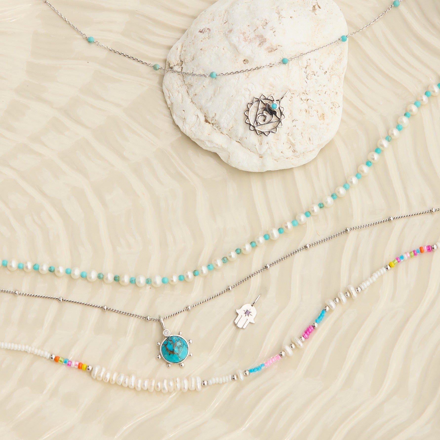 sterling silver jewellery pieces displayed on textured  surface including the Pearl & Turquoise Necklace Sterling Silver