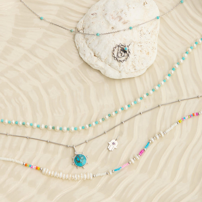 sterling silver jewellery pieces displayed on textured  surface including the Pearl & Turquoise Necklace Sterling Silver