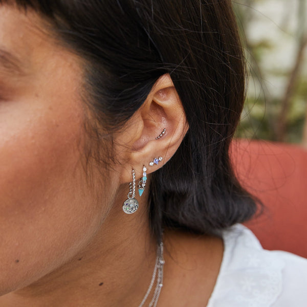 close up of the Medium Twisted Huggie Hoop Earring Sterling Silver on model ear with coin charm