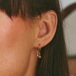 Close-up of an ear wearing a gold hoop earring with a small moon and star charm.