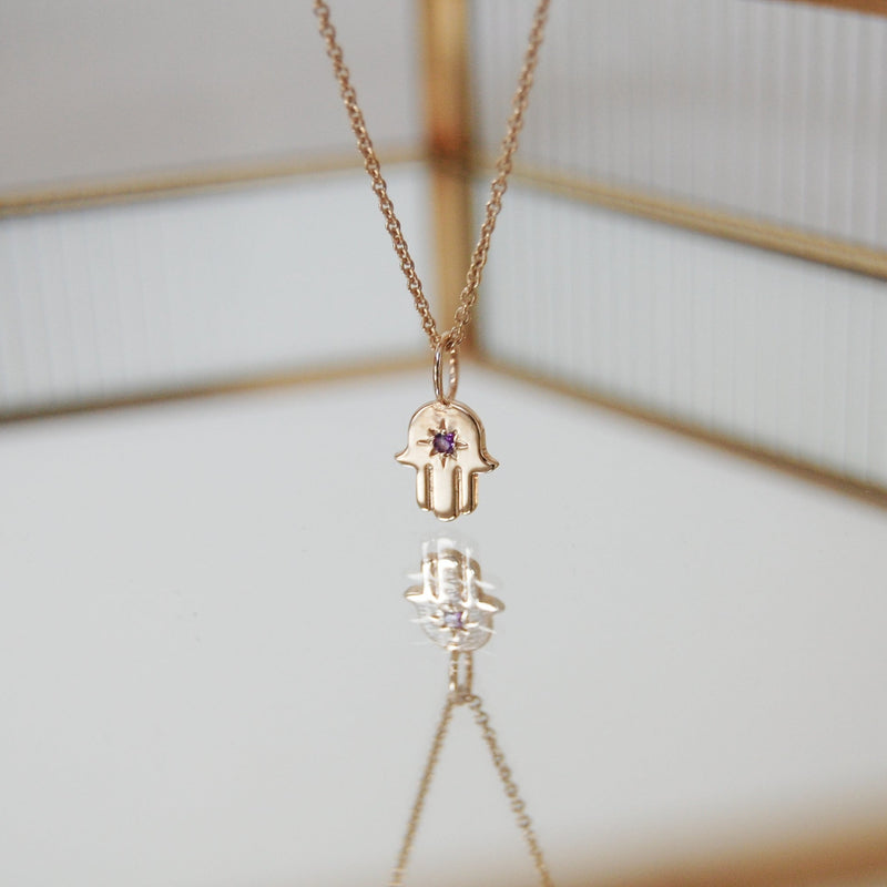 solid gold amethyst hand of fatima pendant and it's reflection in mirror jewellery box