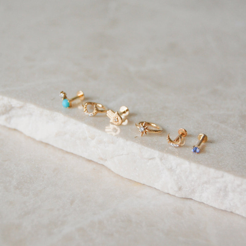 yellow gold earring display on marble surface including the Mini Tanzanite Solitaire Flat Back Earring 9k Gold