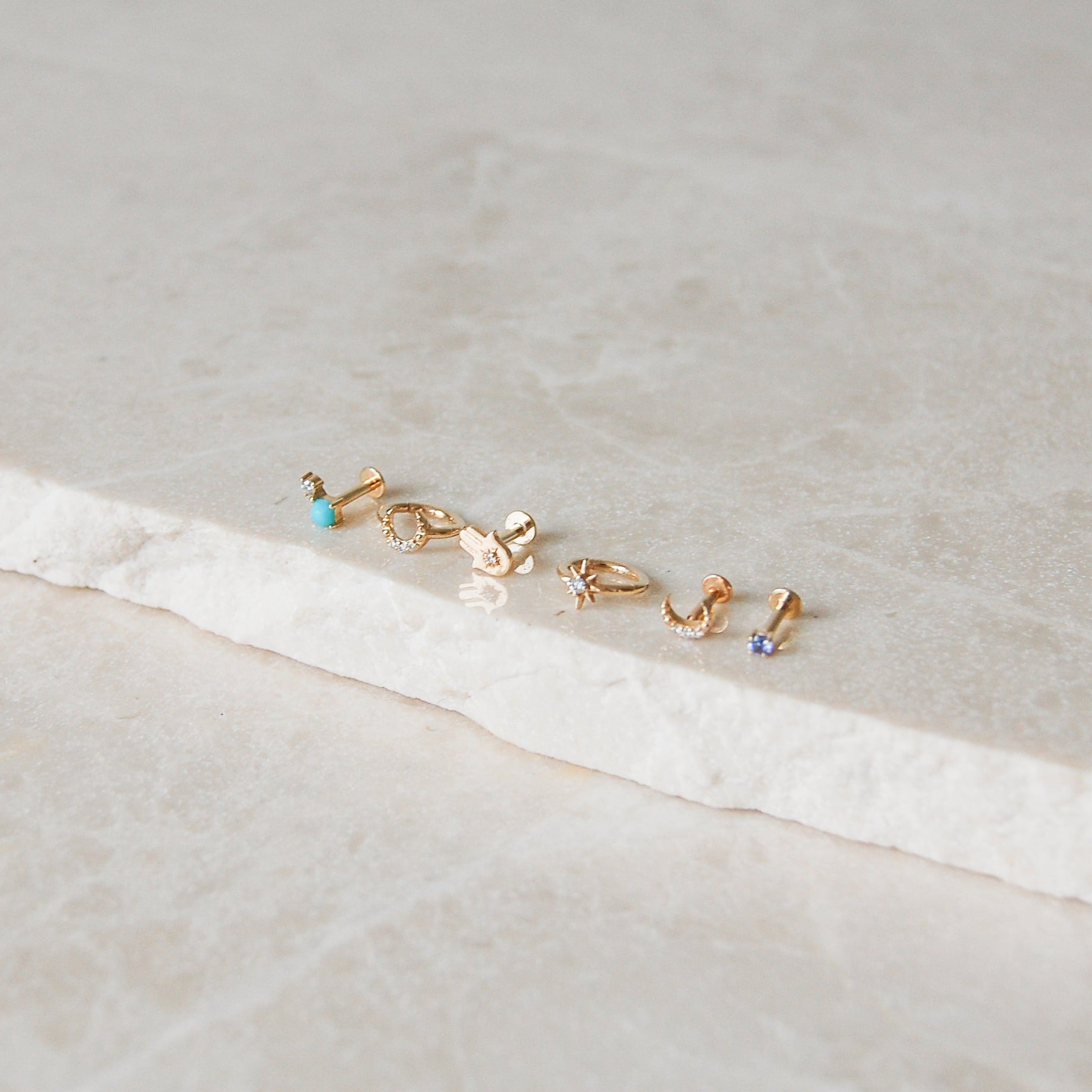 gold earring display on marble surface including the Turquoise & Diamond Flat Back Earring 9k Gold