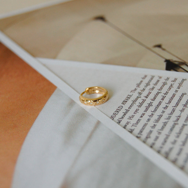 Diamond Engraved Huggie Hoop Earring 9k white Gold displayed on top of papers