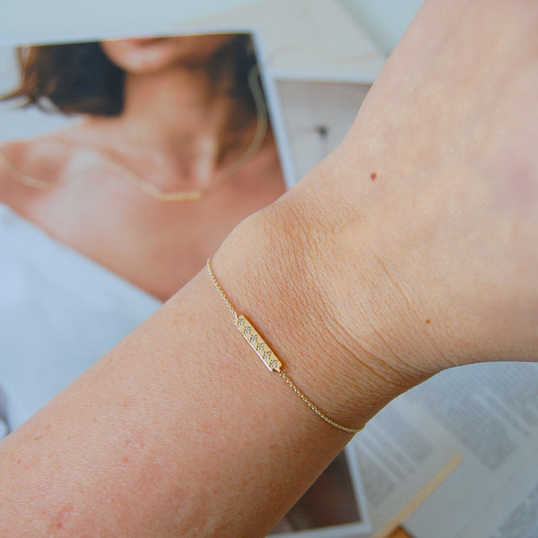 Diamond Bar Bracelet 9k Gold on wrist and matching necklace on the background on printed paper