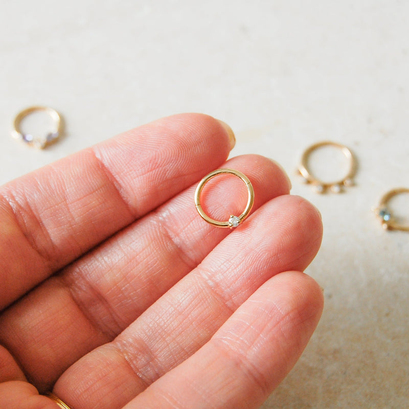 hand holding a diamoond solitaire 14k gold hoop for daith piercings
