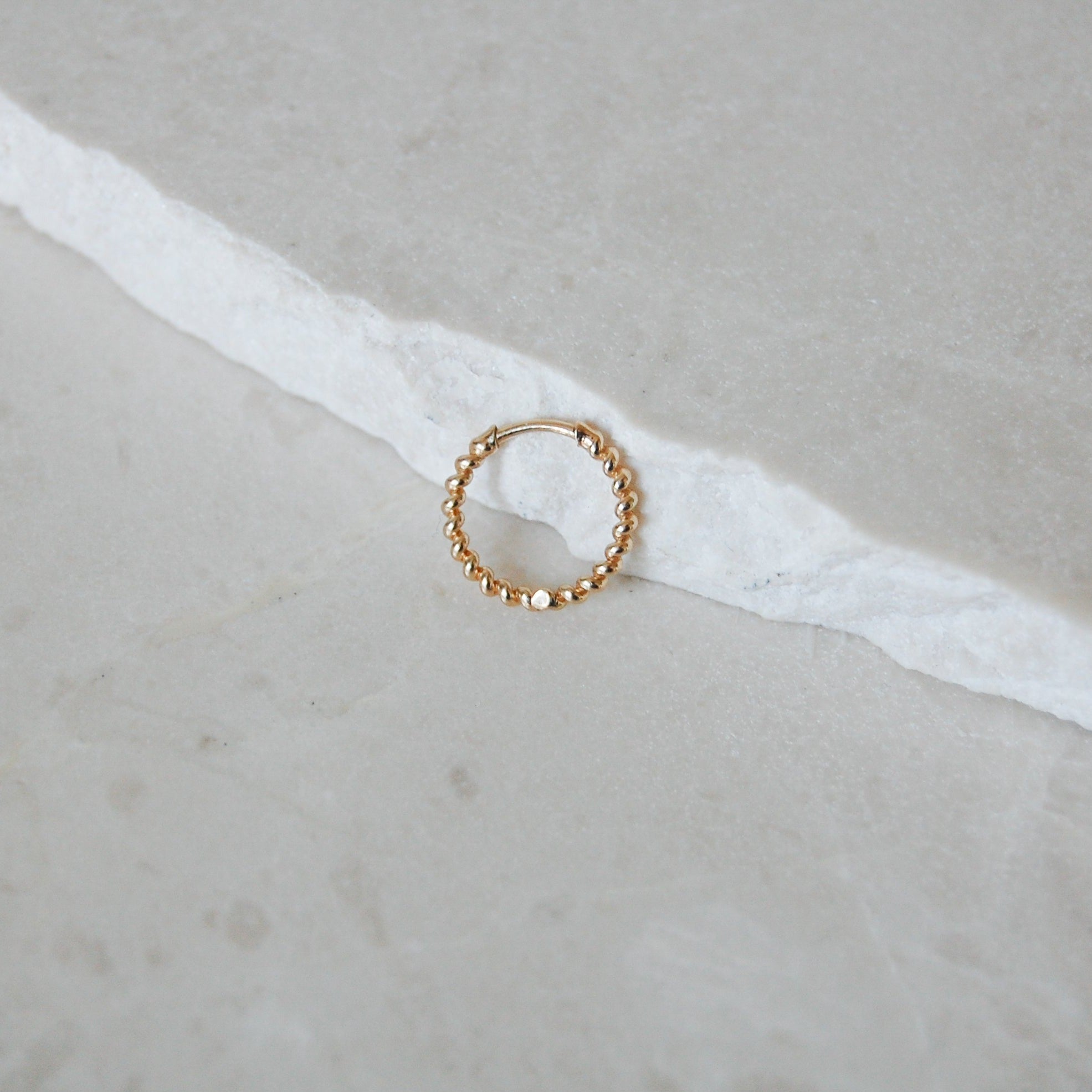 Medium Twisted Huggie Hoop Earring 9k Gold on marble surface