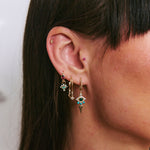Close-up of an ear wearing gold earrings with gemstones against a neutral background