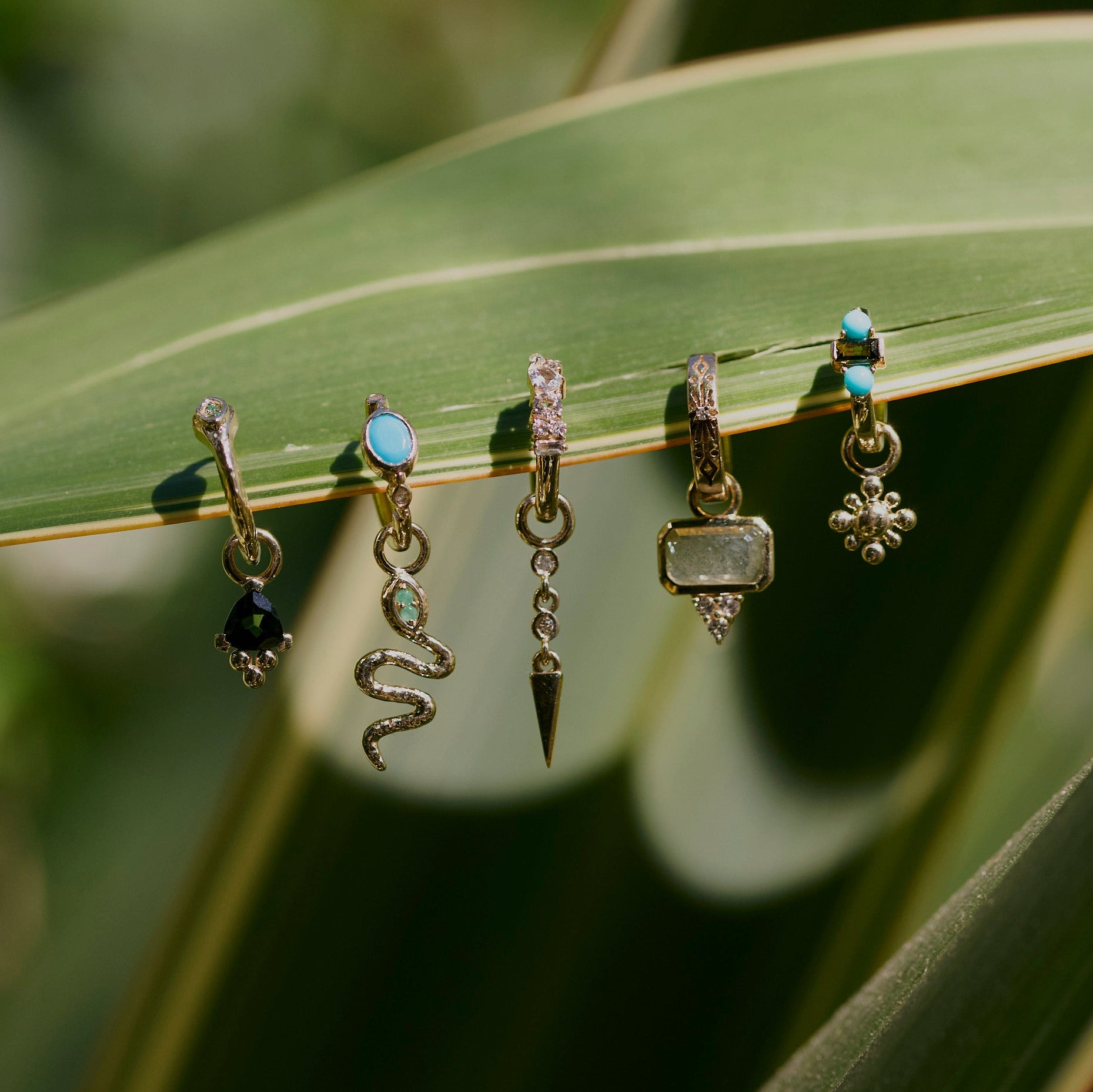 Diamond Drop Spike Earring Charm 9k Gold displayed from a green leaf along with other solid gold earrings and charms