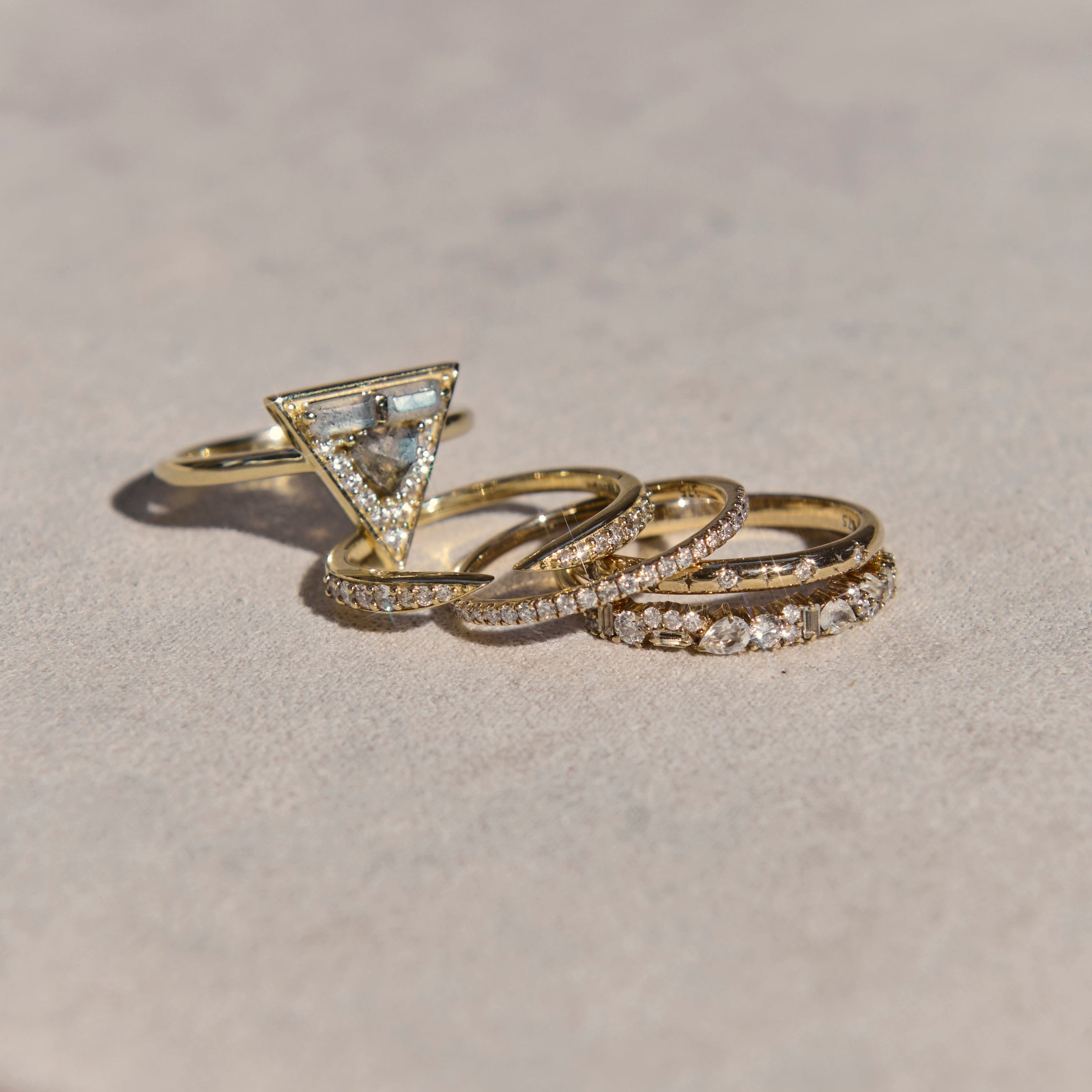 Three gold rings with diamond accents on a light pink surface