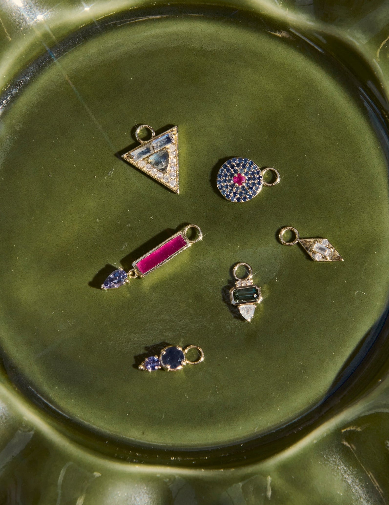 Green ceramic dish with small jewelry items on a beige surface