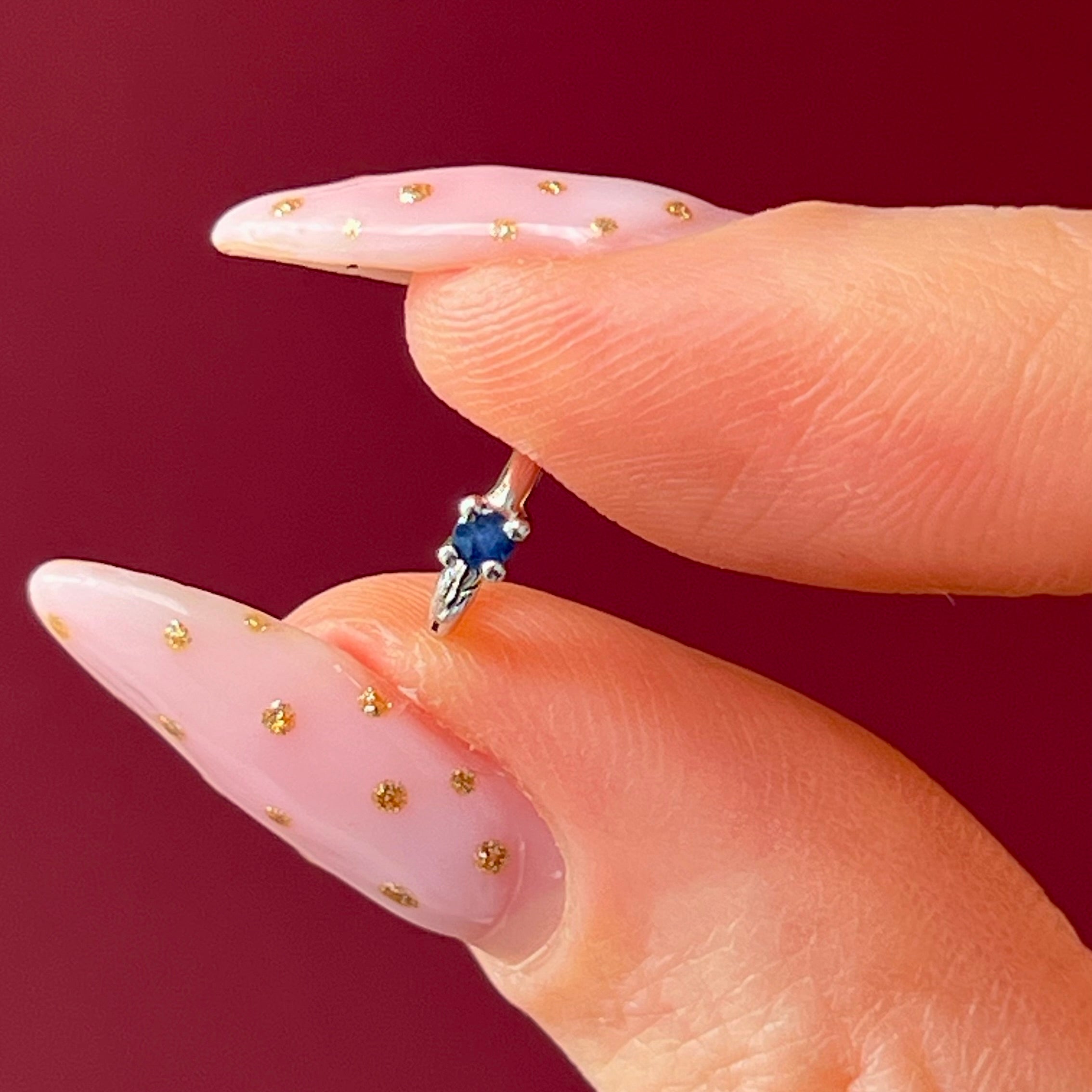 Close-up of a hand with a ring featuring a blue gemstone against a red background