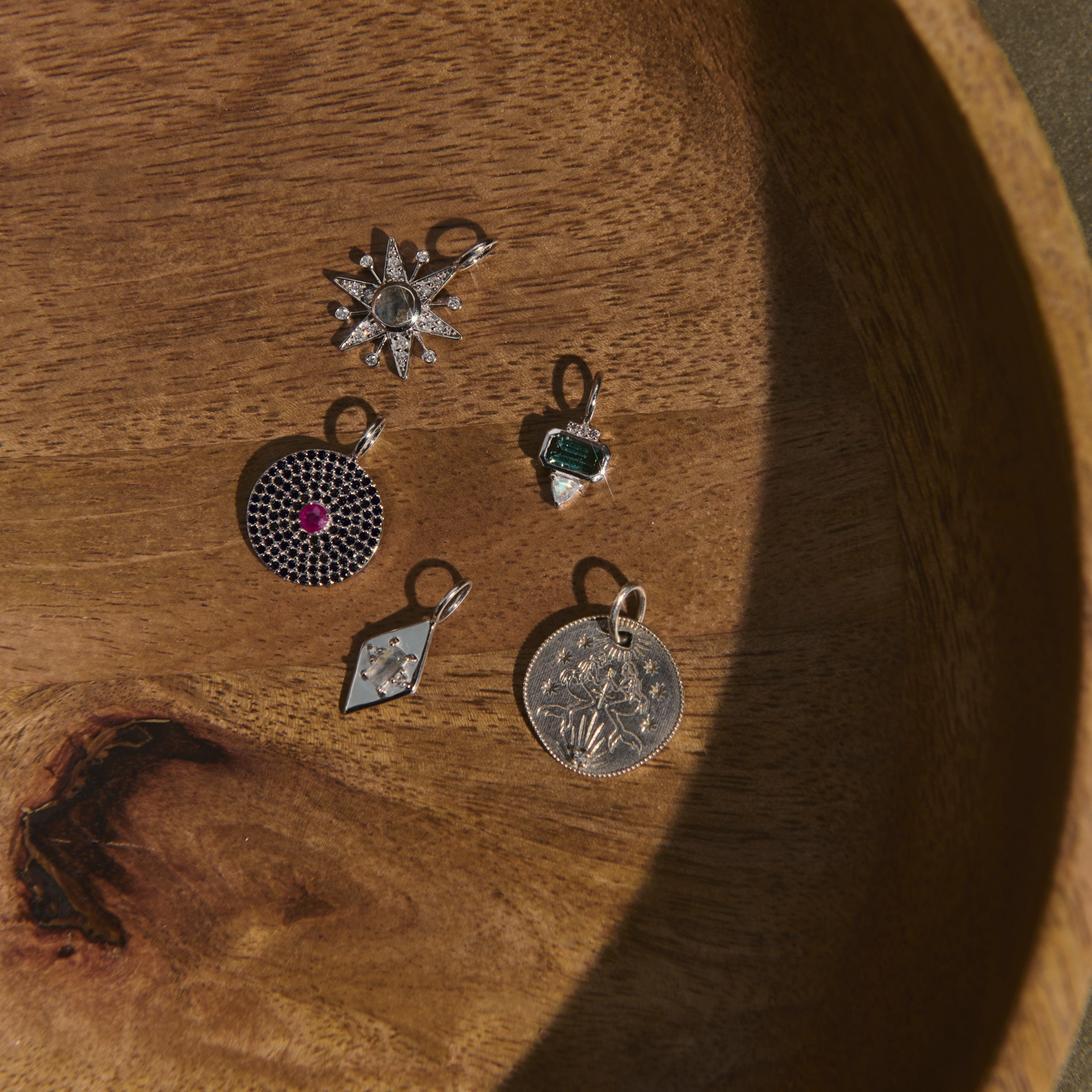 Five silver pendants on a wooden surface