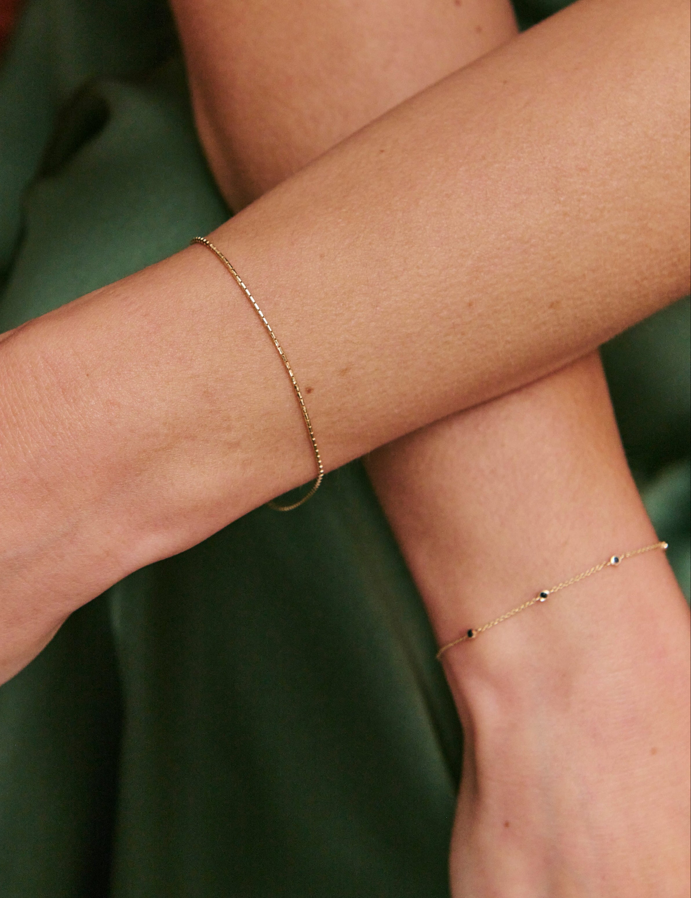 Two arms with gold bracelets against a green fabric background