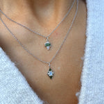 Two silver necklaces with green gemstone pendants on a person's neck against a white background.
