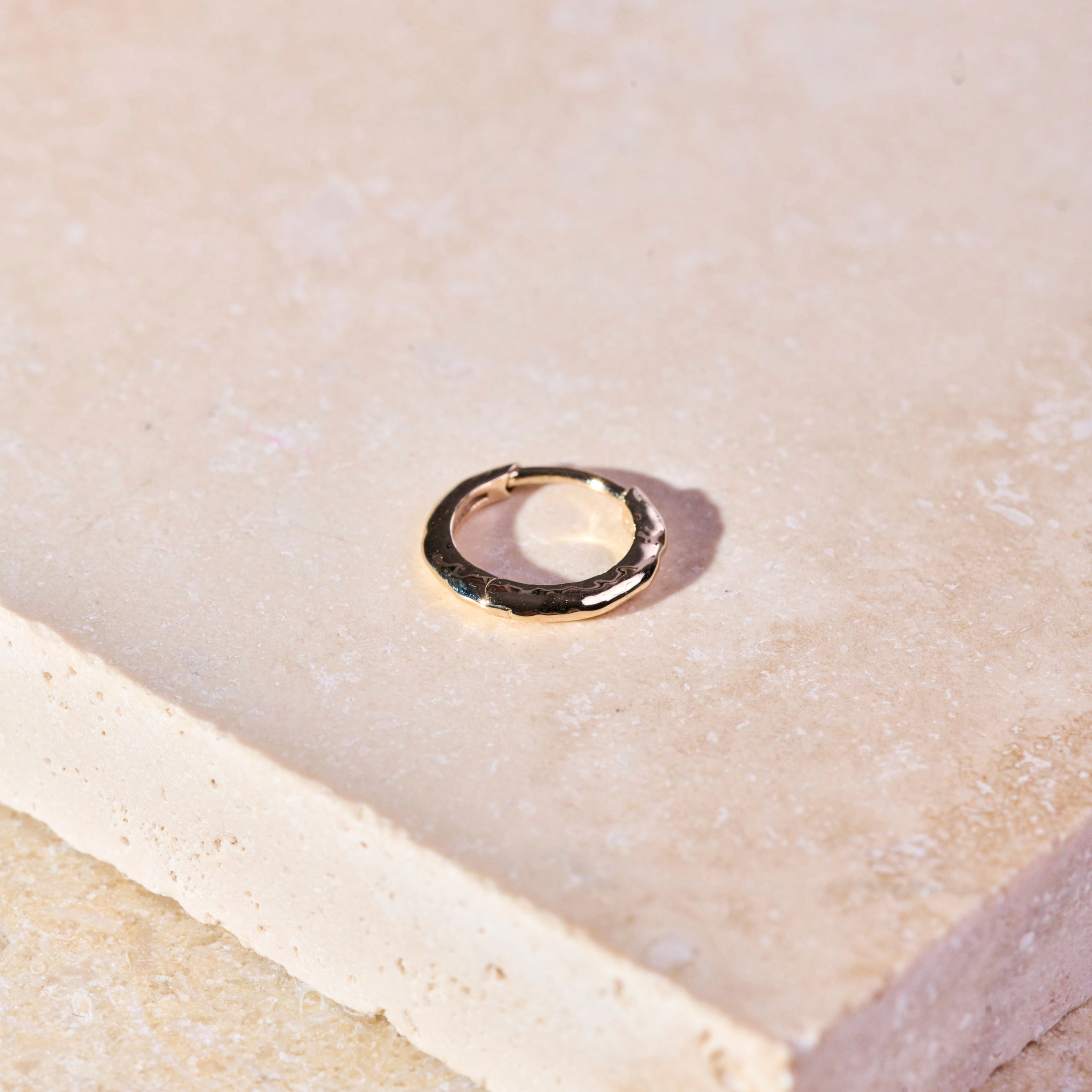Hammered Huggie Hoop Earring 9k Gold on hard surface
