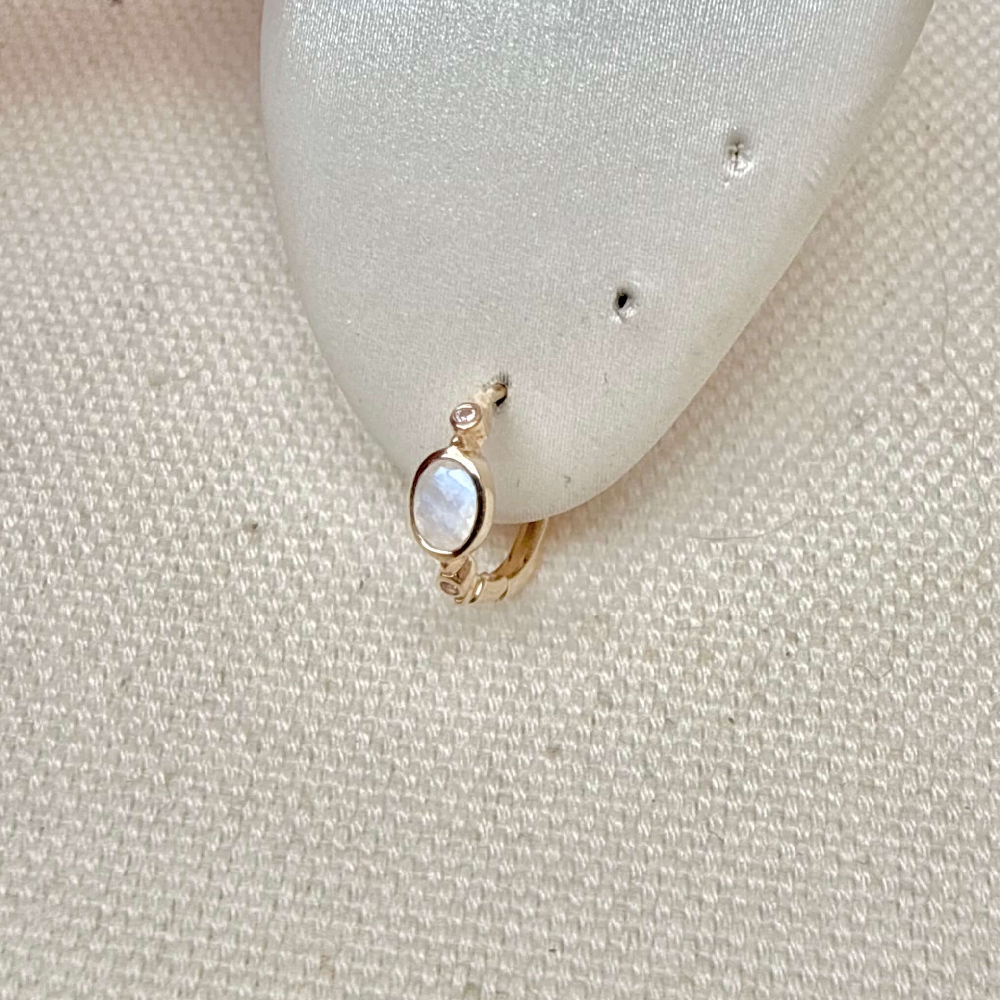 Gold earring with a small stone on a textured beige surface