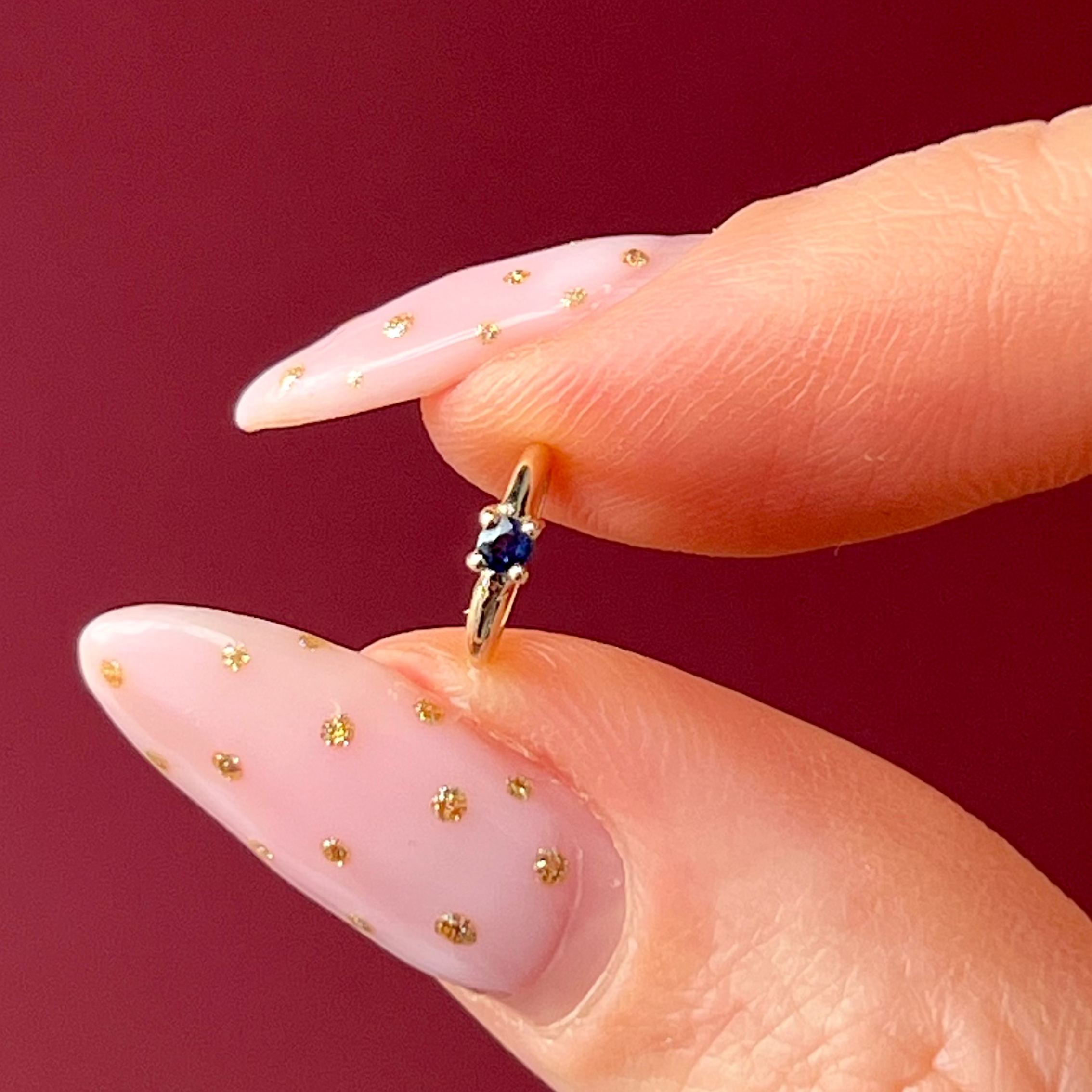 Close-up of a hand with a gold ring featuring a blue gemstone against a red background