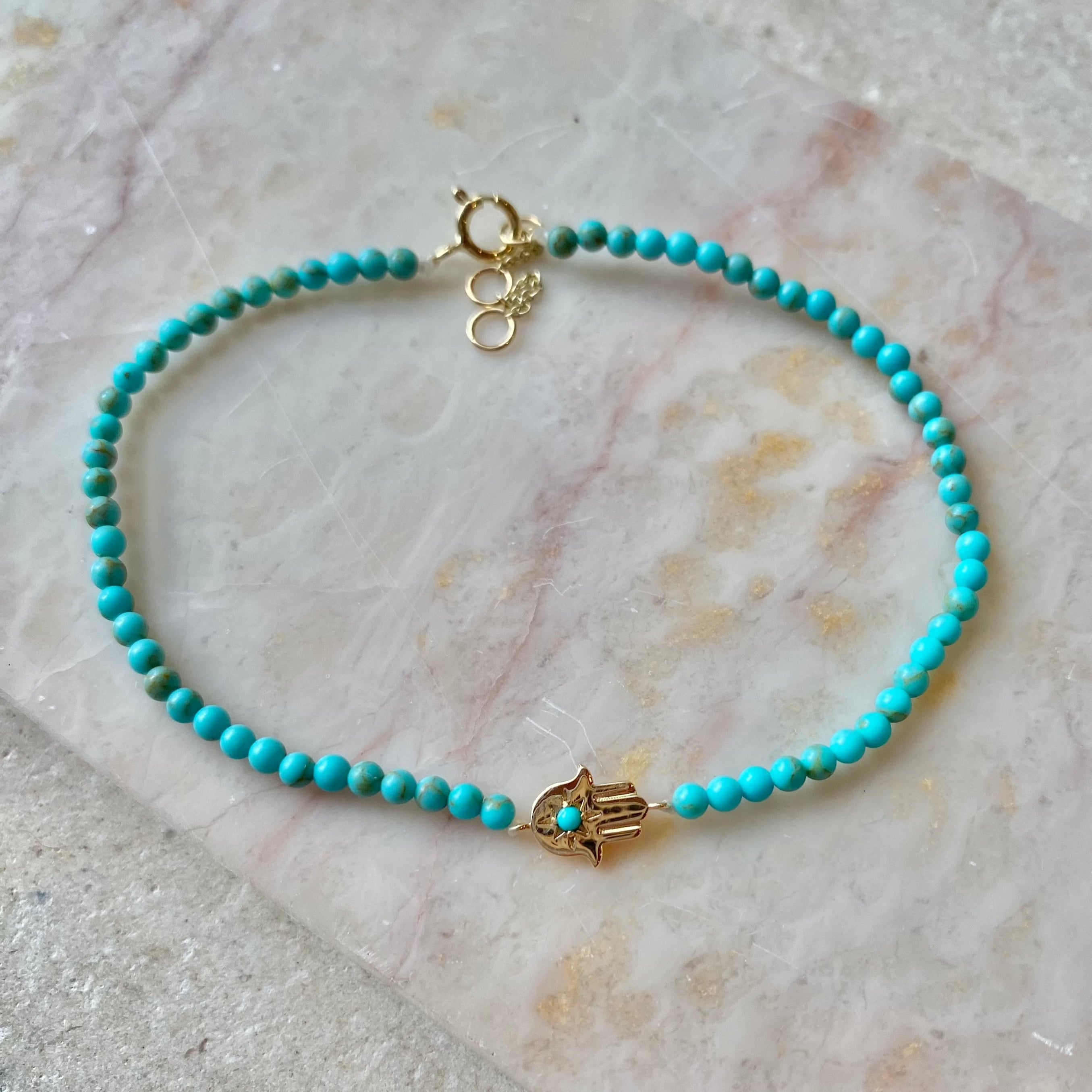 Hand of Fatima Turquoise Beaded Bracelet 9k Gold on hard marble surface