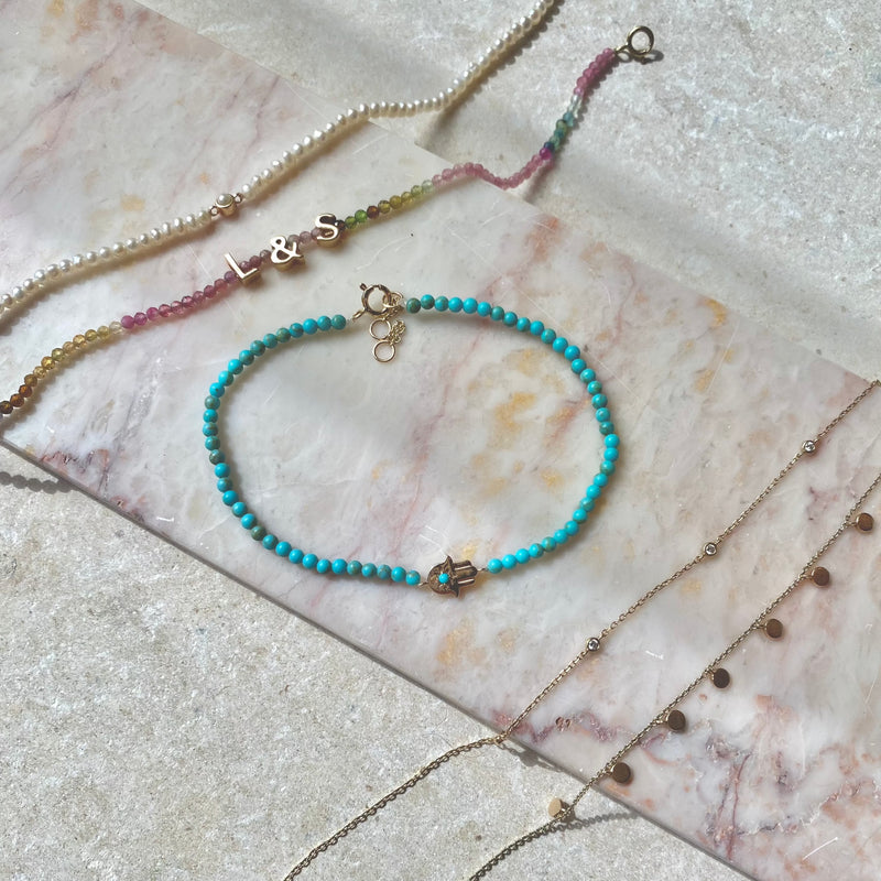 solid gold bracelets displayed on marble surface including the Hand of Fatima Turquoise Beaded Bracelet 9k Gold