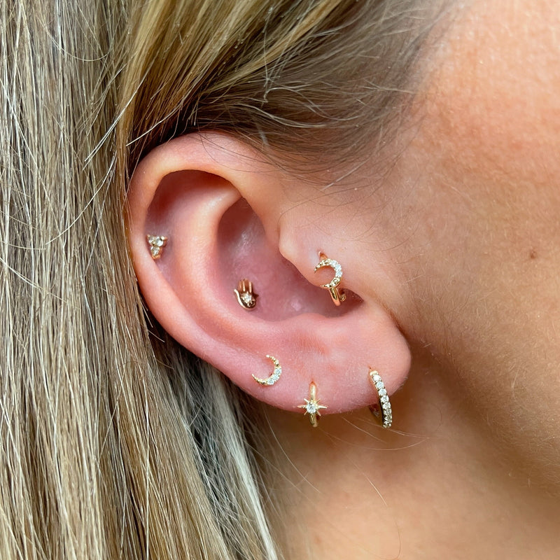 model wearing earring stack including the Diamond Moon Seamless Huggie Hoop Earring 9k Gold on tragus