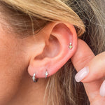 model wearing earring stack and the Diamond North Star Seamless Huggie Hoop Earring White 9k Gold on second lobe piercing