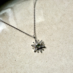 white gold necklace with a star-shaped pendant on a textured beige surface