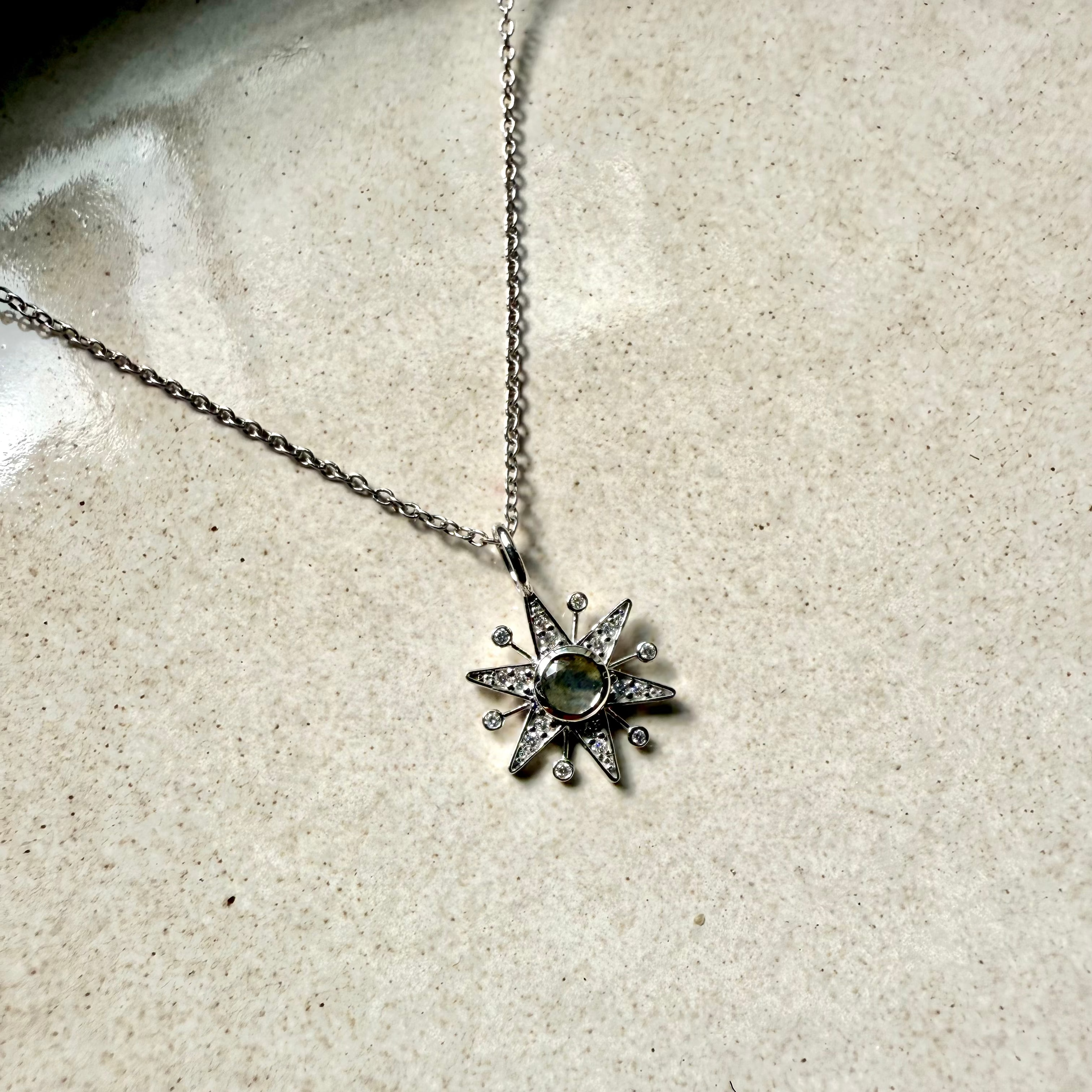 white gold necklace with a star-shaped pendant on a textured beige surface
