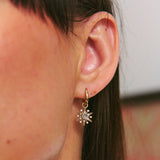 Close-up of an ear wearing a gold star-shaped earring with a gemstone.