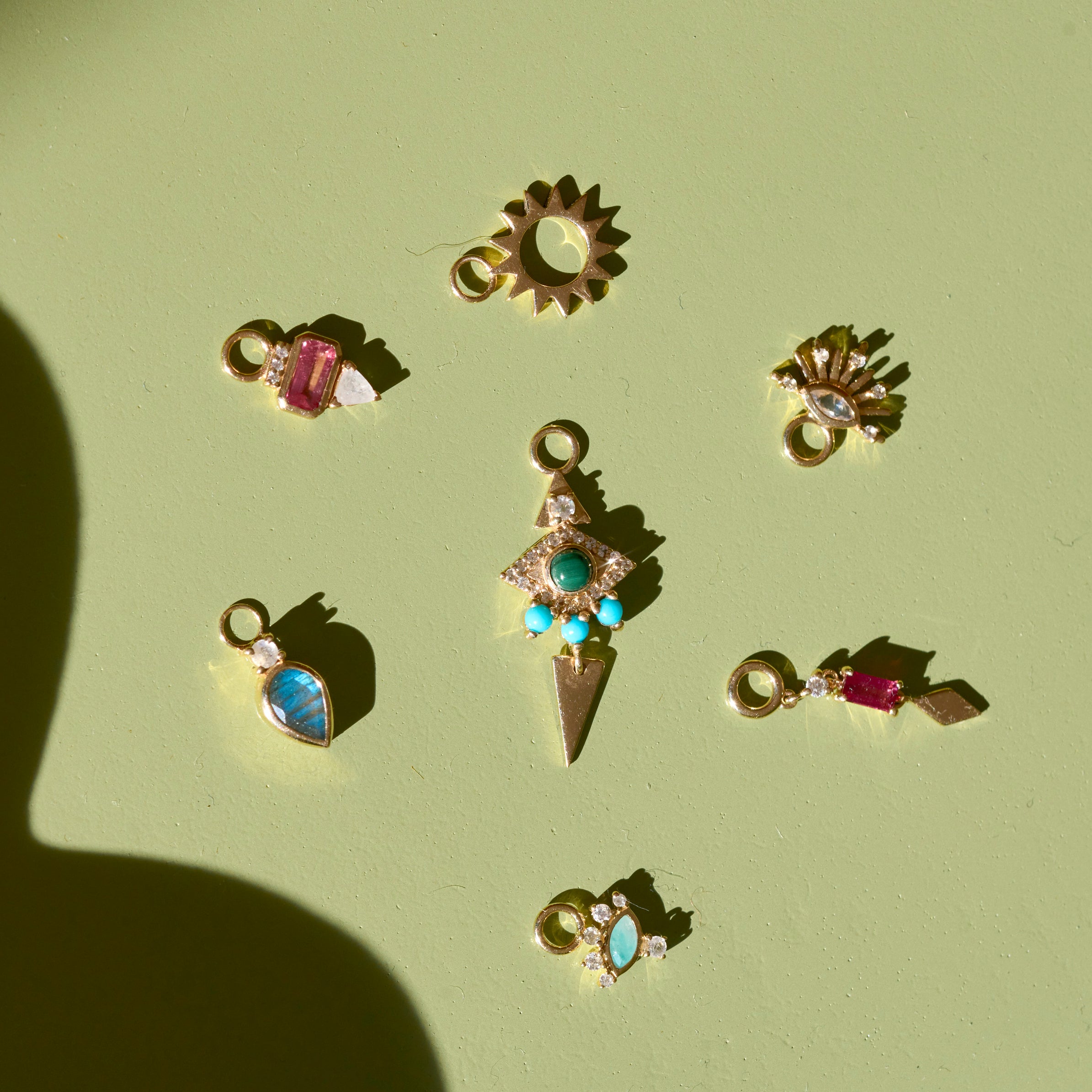 solid gold earring charms on green surface including the Limited Edition Malachite Eye Hoop Earrings 9k Gold