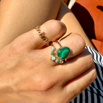 Close-up of a hand wearing two rings with green and blue gemstones.