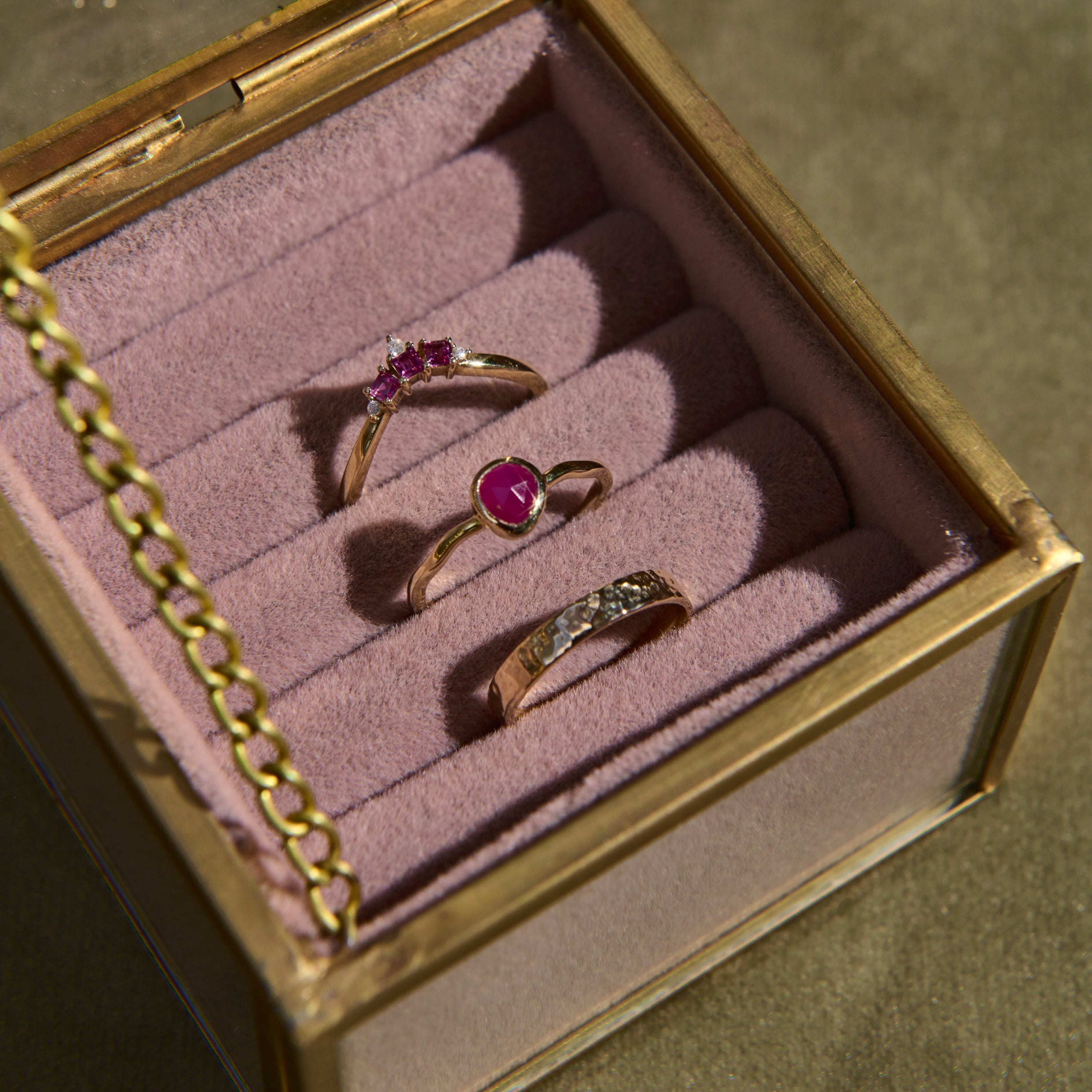Three rings with gemstones in a jewelry box on a textured surface