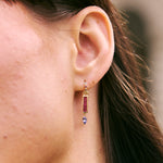 Close-up of an ear wearing a gold earring with a pink gemstone.