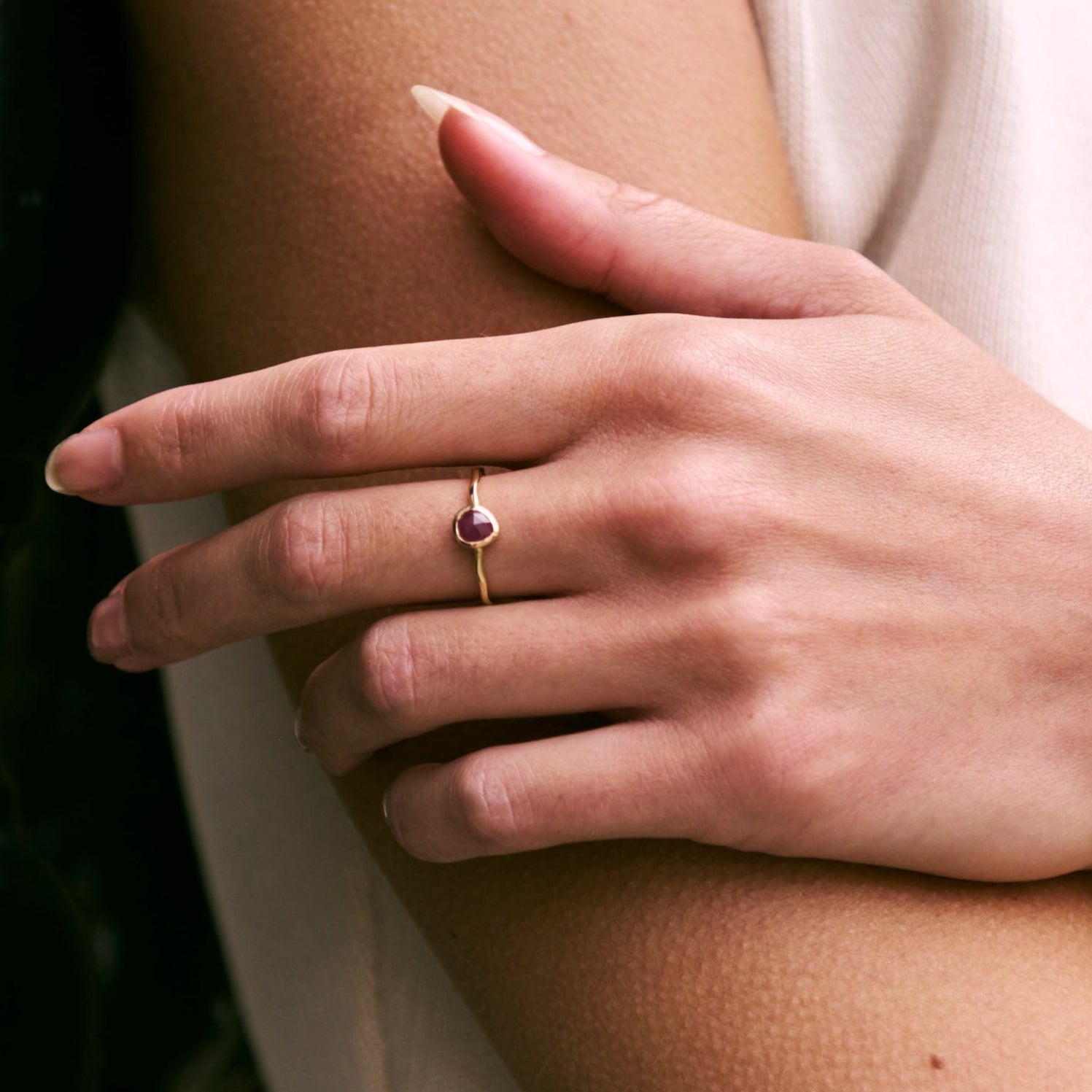 Hand wearing a gold ring with a red gemstone on a blurred background
